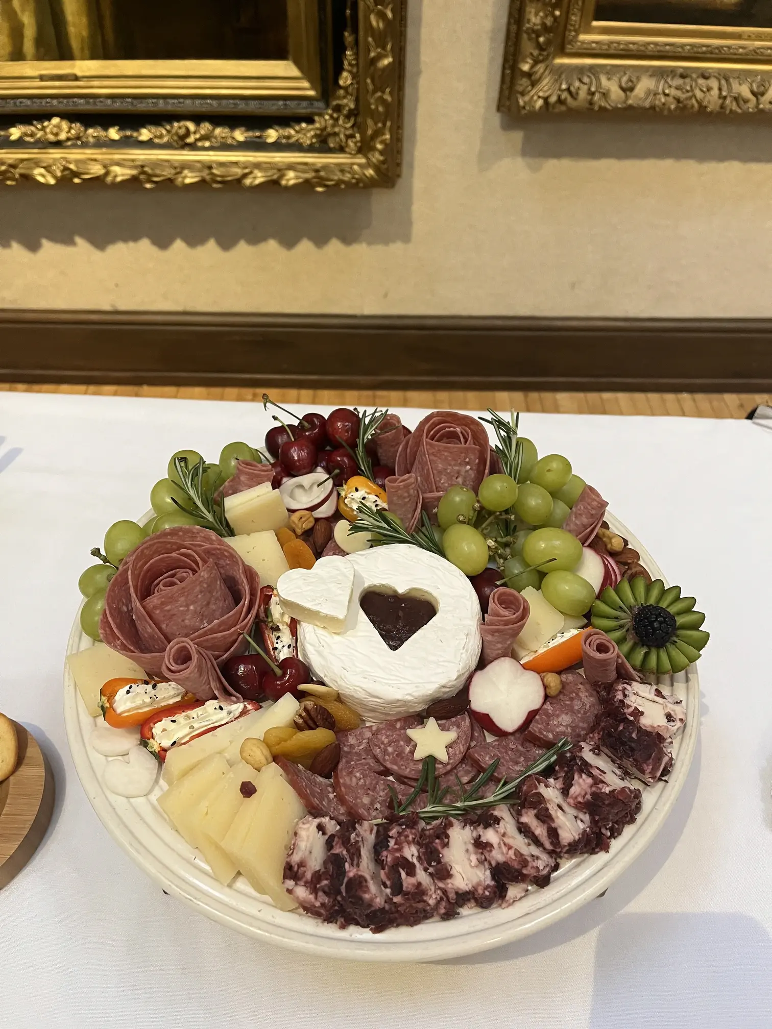 A charcuterie board with a round cut of brie in its center. A heart shaped piece of brie is cut from its center.