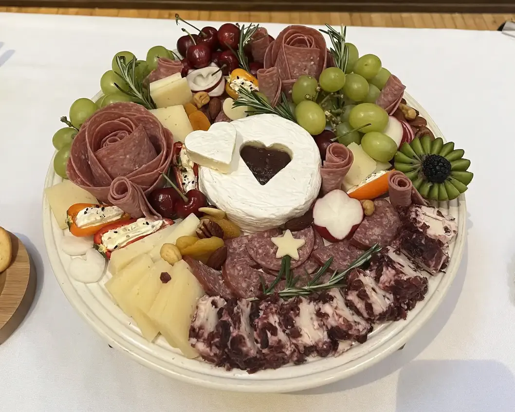 A charcuterie board with a round cut of brie in its center. A heart shaped piece of brie is cut from its center.